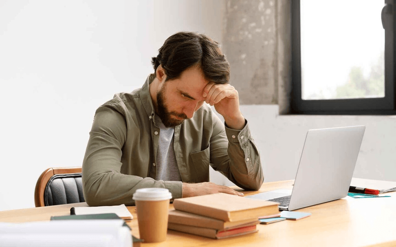 Photo of a visibly stressed professional sitting at a desk piled high with papers, looking overwhelmed by their computer screen displaying emails